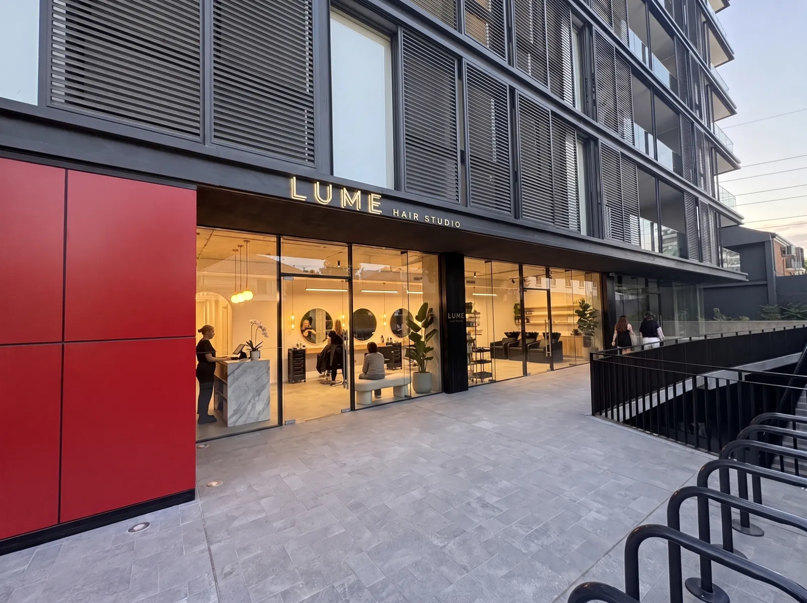 Fachada iluminada de un salón de belleza con recepción de mármol y lavatorios al fondo