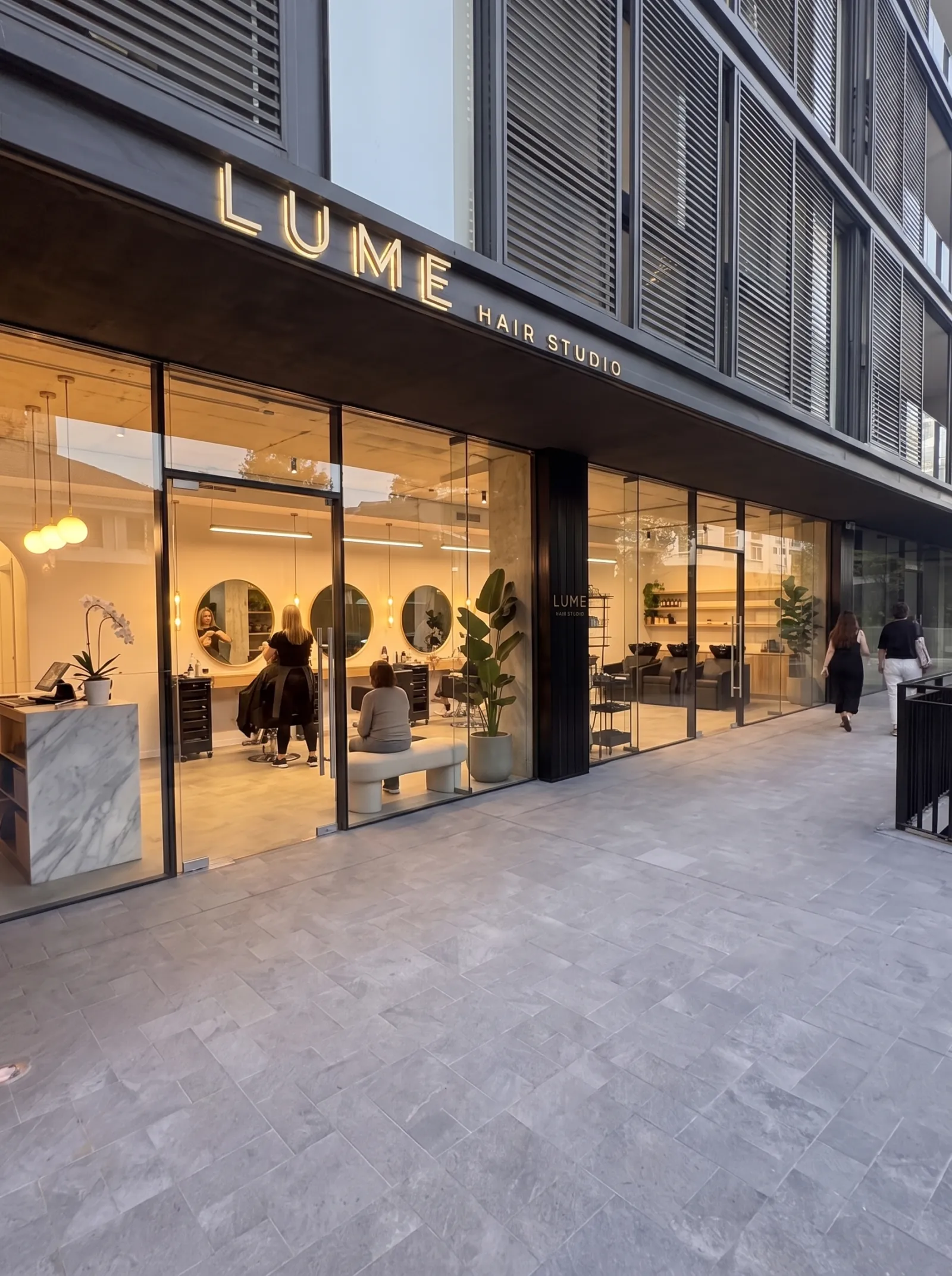 Salón de belleza visto desde el paseo, con estaciones de peinado y espejos circulares