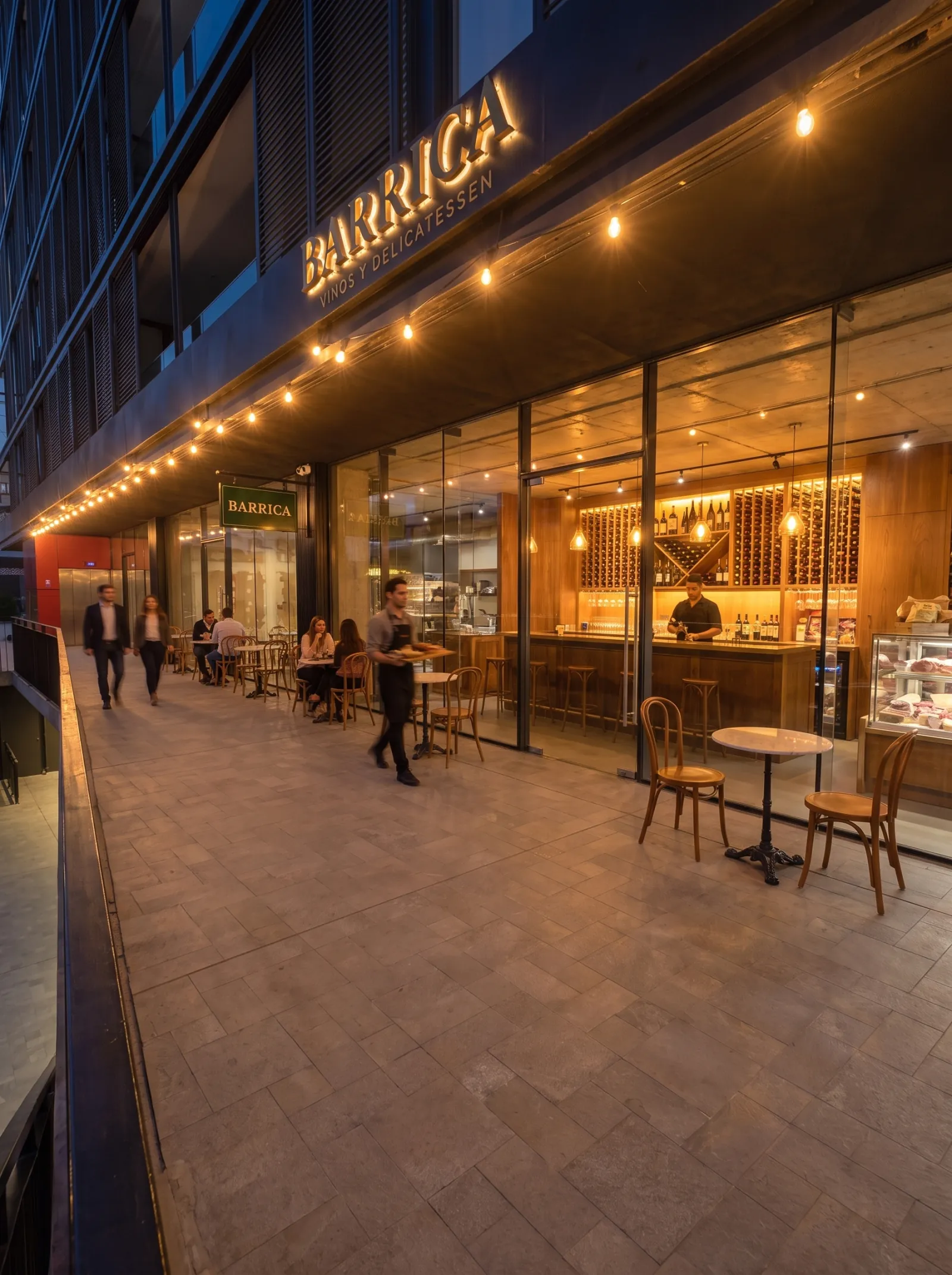 Tienda de vinos y delicatessen con mesas en el paseo exterior al anochecer
